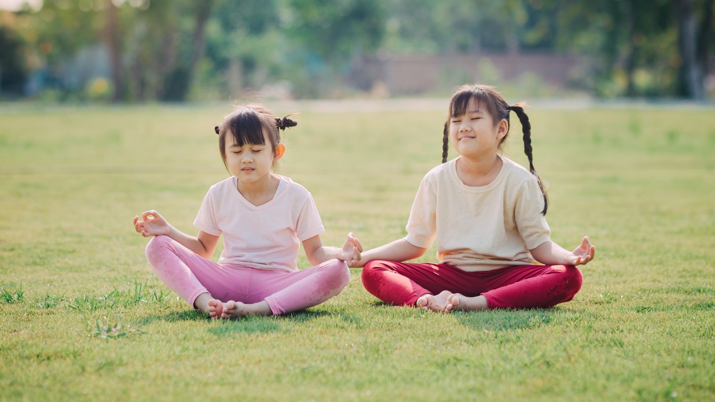 Children meditation with yoga pose on green grass field.